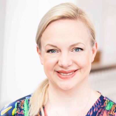 Woman with blonde hair and a colorful top against a neutral background