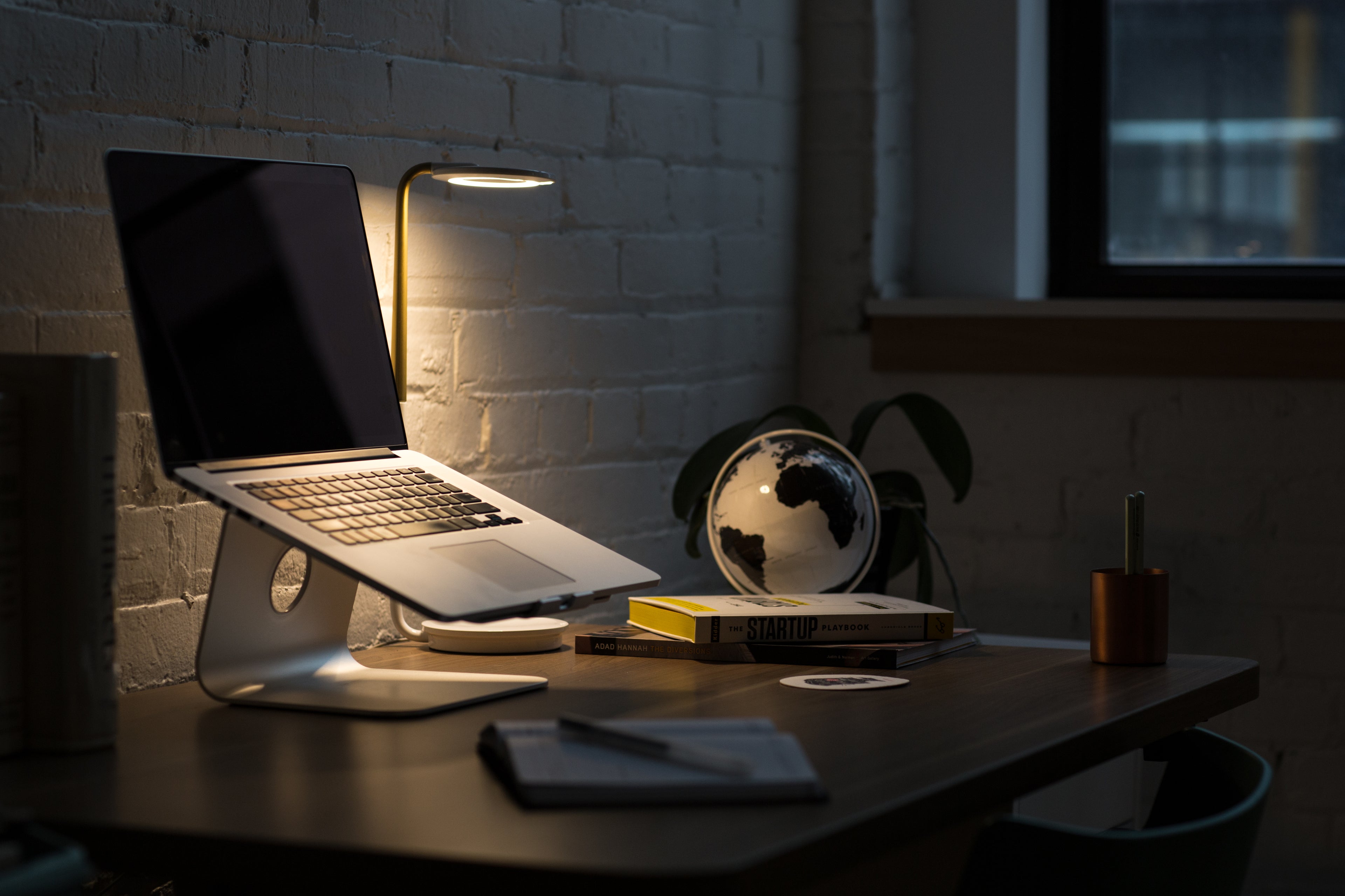 laptop on a desk at night with a desk lamp and globe